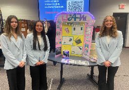  three students stand by their project display board